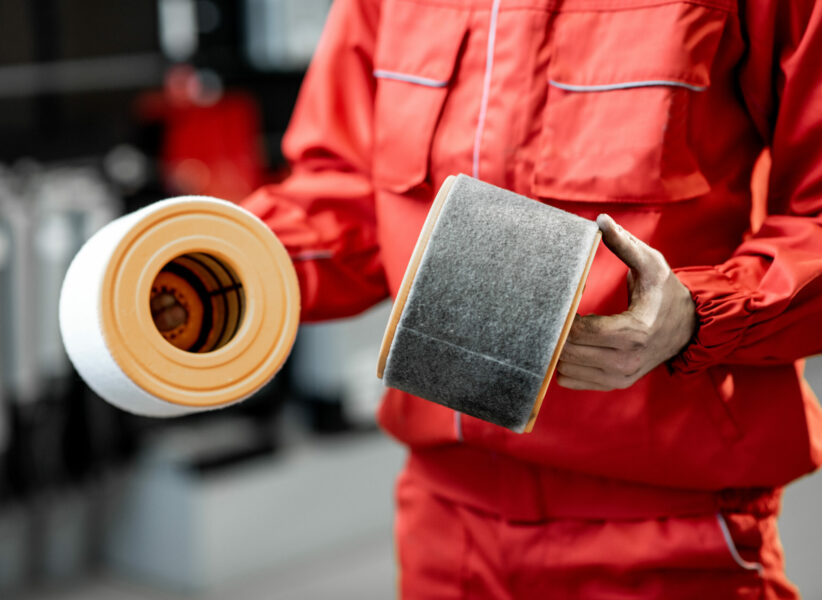 Auto mechanic in red uniform holding new and used air filter standing at the car service, close-up view with no face