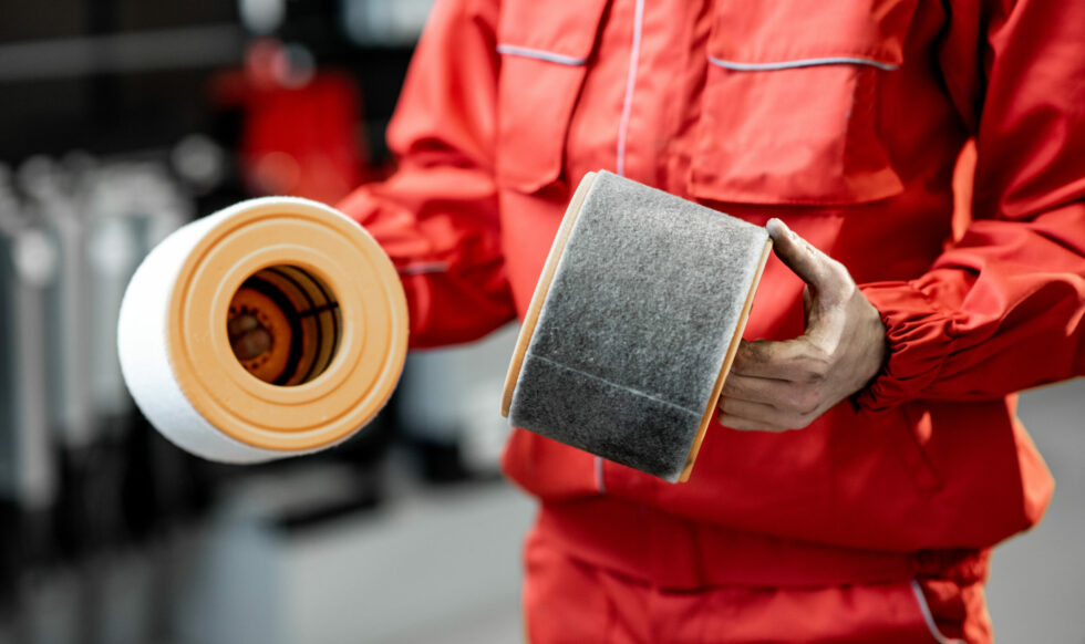 Auto mechanic with new and used car air filter Auto mechanic in red uniform holding new and used air filter standing at the car service, close-up view with no face